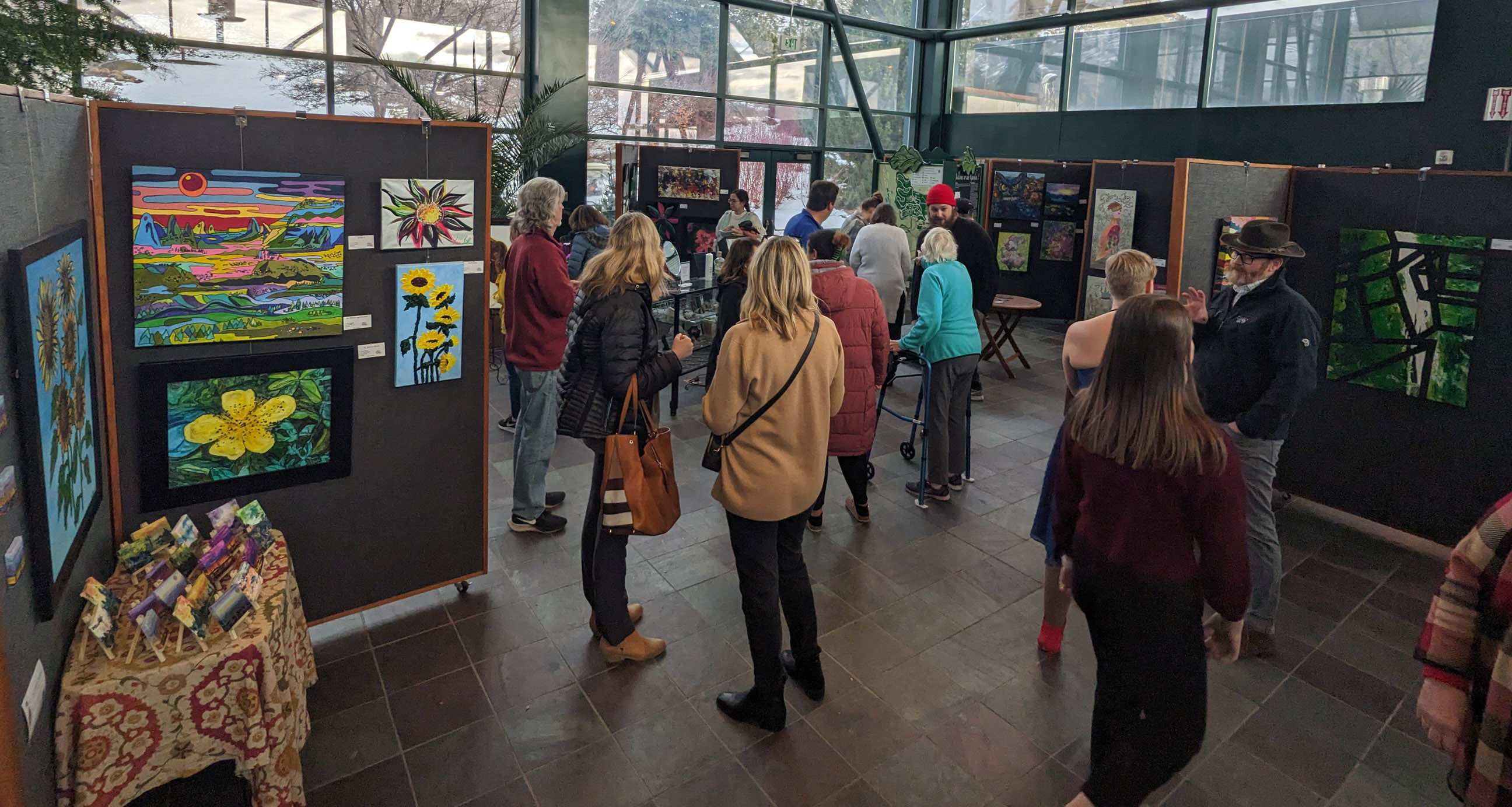 A crowd mingling with artists. Paintings are hung on modular panels spread throughout the room.